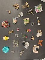 Full display of 26 assorted brooches and pins including floral designs, animal shapes, and rhinestone tiger on black surface.