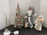 Photo showing all four items together: two Santa figures, silver Christmas tree cone, and small light-up tree