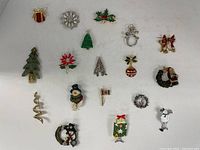 Top view of all 16 Christmas-themed brooches arranged on flat surface.