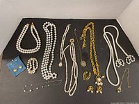 Full view of tray showing multiple faux pearl necklaces, earrings, bracelet, and brooch on black background inside box.