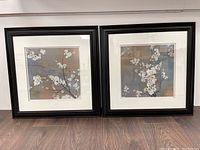 Pair of square framed art prints featuring cherry blossom branches with white flowers, framed in black with white mats.