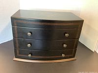 View of the black wood jewelry box showing the front side with two drawers, each drawer having two metal knobs.