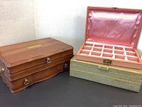 Closed brown leather jewelry box with three metal clasps and brass plate on top, next to an open wood jewelry box.