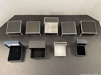 Five closed dark brown square jewelry boxes with white trim on top, displayed in a single row, with one center box open showing white interior.