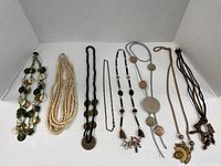 Full view of all eight long necklaces displayed side by side showing various natural materials including wood, stone, shells, different bead shapes and pendant details.