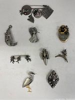 Full collection of brooches and pins arranged on white background, showing variety of shapes and themes.