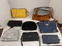 Nine small purses, wallets, and makeup bags arranged on a white surface including leather and fabric materials.