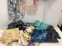 Photo of the assortment of shawls and scarves laid flat and stacked to show different colors and designs, including butterfly and floral patterns.
