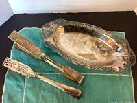 Full view of vintage silver tray with two silver-plated tongs on a teal cloth background