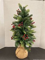 Full view of 24 inch tall faux Christmas tree with pine cones, red berries, and burlap wrapped base.