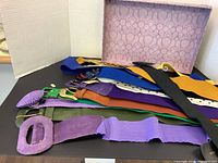 Assortment of colorful vintage ladies belts displayed with varied buckle designs and a patterned box in the background.