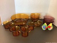 Overview of all items in the lot including amber glass mugs, bowls, cranberry bowls and salt and pepper shakers
