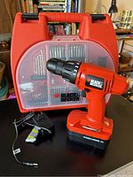 Black & Decker cordless drill with charger and plastic case containing drill bits and accessories.