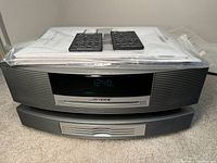 Stacked Bose Wave unit and CD changer with remotes and manuals on top