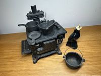 Photo showing the miniature cast iron stove with cooking accessories arranged on and around it, including the ceramic bird figurine adjacent.