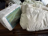 Packaged white silk duvet in carry bag labeled Royal Elite Silk Duvet next to unbagged white down duvet