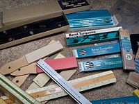 Overall view of vintage Berol Turquoise pencils and leads in original boxes, wooden and metal rulers, and straight edge tools on carpeted floor