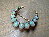 Front view of crescent brooch displaying 13 opals in graduated sizes