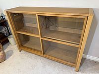 Front view of the Ikea Edefors display cabinet showing two sliding glass and wood doors closed, four glass shelves visible inside, light wood finish.