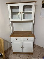 Full front view of kitchen cabinet microwave stand showing white painted frame, wood grain counter and base, glass panel doors on upper cabinet and wooden doors on lower cabinet.