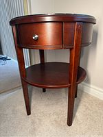Front angled view of the wooden round lamp table showing drawer and lower shelf.