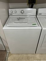 Front view showing Maytag top-load washing machine with white finish, control panel with dials, and user manual on top.