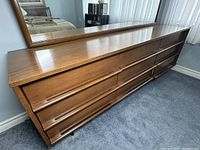 Front angle view of walnut dresser with mirror, showing all nine drawers and integrated pulls.