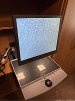 Front view of the Optelec ClearView+ with screen displaying static noise and reading surface below.