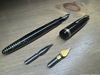 Early Parker fountain pen disassembled with two extra nibs displayed on light wood surface