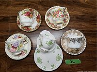 Top view of all five cups and saucers arranged on a wooden floor, showing colorful floral designs and shapes.