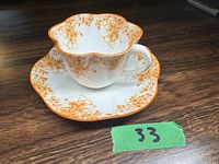 Porcelain cup and saucer shown together on wooden surface with green numbered tag.