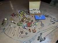 Overview of assorted silver and costume jewelry, brooches, pins, and watches on a wooden table including colorful Christmas brooches and a pearl necklace.