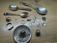 Full layout of sterling silver collectible items showing spoons, rings, pendants, and decorative pieces arranged on a wooden surface.