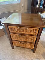Front view of the table showing all three wicker drawers closed in a wooden frame.