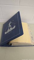 Blue baseball card album binder with 'Baseball Card Album' text and baseball player silhouette on cover.