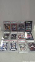 Full view of 12 graded football trading cards laid out on a flat surface, showing various players and grades.