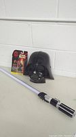 Darth Vader mask, Star Wars Episode 1 action figure in package, and light-up lightsaber laid out on a table.