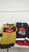 Two jerseys laid flat on a surface, gold Winnipeg Falcons Team Canada and black Team Canada hockey jersey.