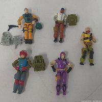 Photo showing five vintage 1980s G.I. Joe action figures on white surface with accessories like helmets and backpacks.