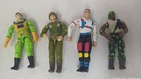 Four G.I. Joe action figures laid out including Flint, Heavy Duty, Col Jet plane Johnson, and an Action Soldier figure
