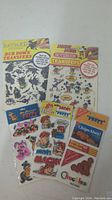 Photo showing a sheet of Batman rub down transfers and a Disney notebook transfers sheet featuring Mickey Mouse and other characters, along with Marvin and Nabisco puffy stickers in packaging.