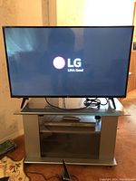 Front view of 43-inch LG TV powered on showing LG logo, sitting on a stand with visible cables and remote.