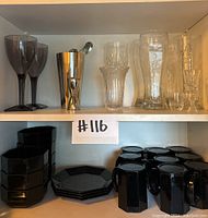 Shelved bar glassware and black dinnerware with a lot number tag