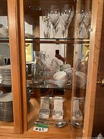 Glassware, plates, teacups, and silverware displayed in wooden glass cabinet.