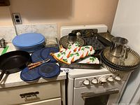 Wide view of the cast iron skillet, reusable food storage containers, oven mitts, and various metal baking pans on the stove and counter.