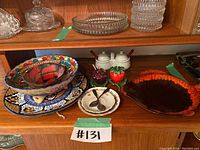 Wide angled photo of entire lot showing colorful vintage servingware items arranged on wooden shelf.