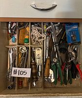 Drawer is divided into compartments holding assorted hand tools and parts, showing various wrenches, pliers, bits, cords, and handles.