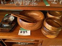 Large wooden salad bowl with a pair of wooden salad servers and small metal trays on wood shelf