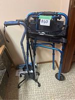 Blue Airgo Hugo walker folded in corner with black fabric seat and backrest strap, front wheels visible.