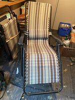One lounge chair unfolded, showing the full reclining design and striped neutral fabric.